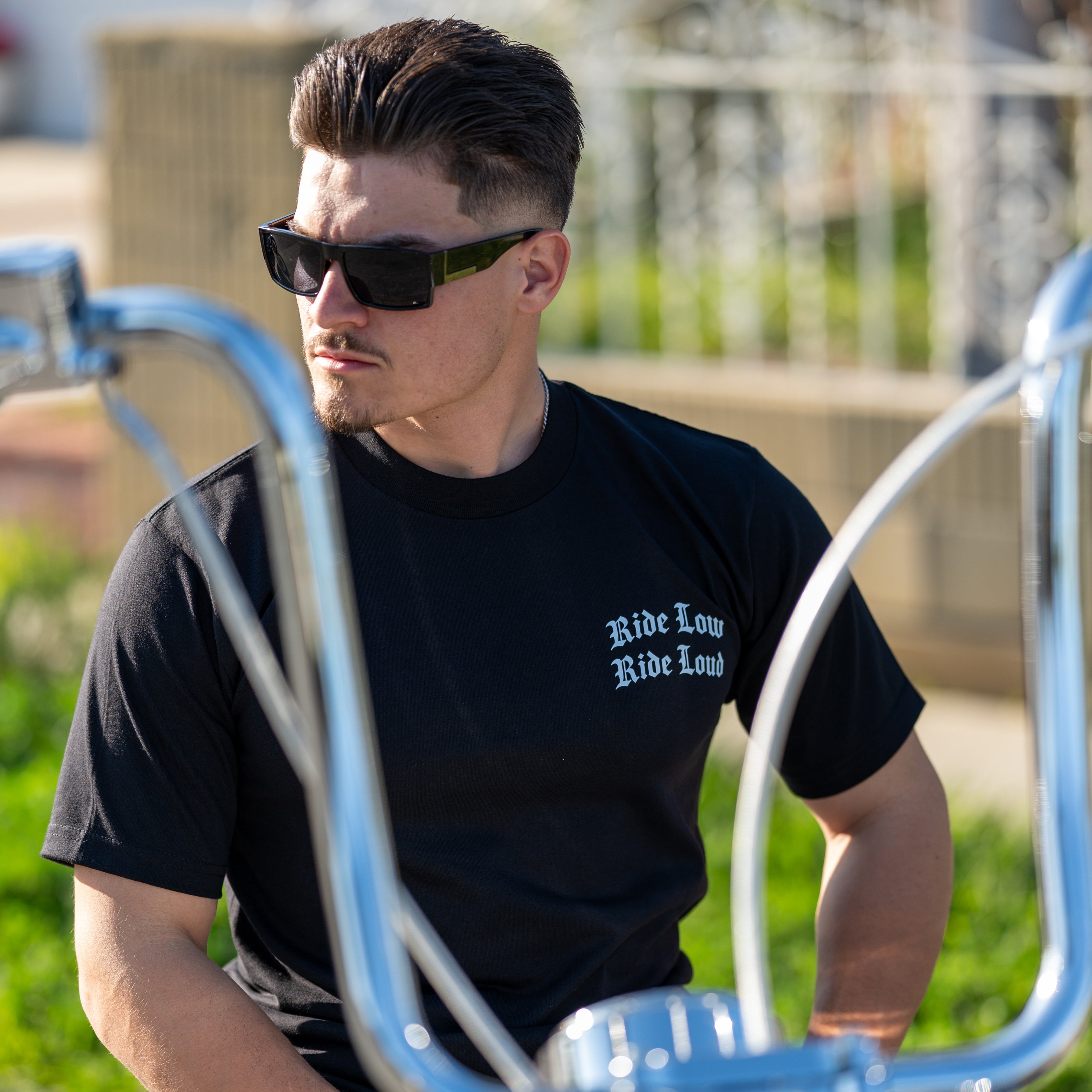 Man wearing sunglasses and a black t-shirt with text, sitting on a motorcycle.